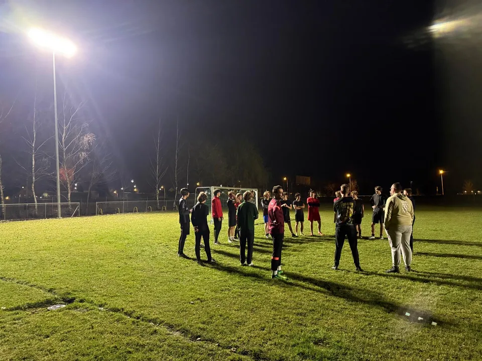 Wieczorny trening reaktywowanej Komety Kryniczno — zawodnicy zebrani na boisku w świetle jupiterów